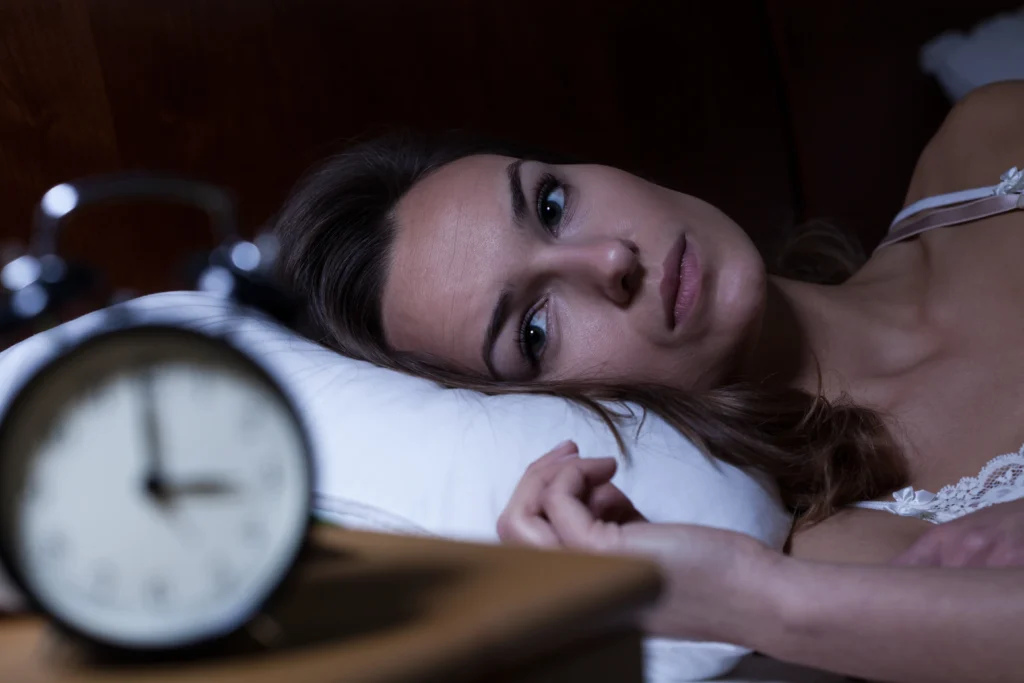 Woman awake at night looking at the clock, illustrating insomnia treatment and difficulty sleeping.